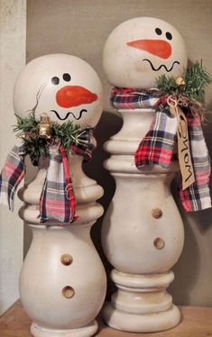 two snowmen standing next to each other on top of a wooden table in front of a wall