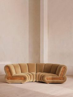 a curved couch sitting on top of a hard wood floor next to a white wall