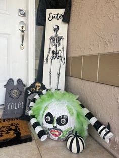 a creepy doll sitting on the ground next to a halloween sign and other decorations in front of a door