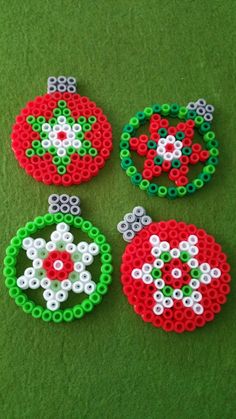 four beaded christmas ornaments sitting on top of a green surface with red, white and green beads