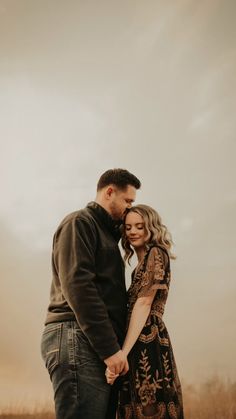 a man and woman holding hands while standing next to each other in an open field