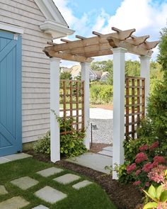 a white house with a blue door and wooden pergolated arbor in the front yard