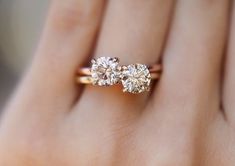 a woman's hand with three stone engagement ring on it and the other hand is holding