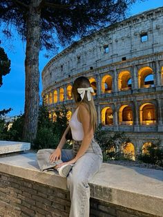 a woman is sitting on a wall in front of the colossion at night