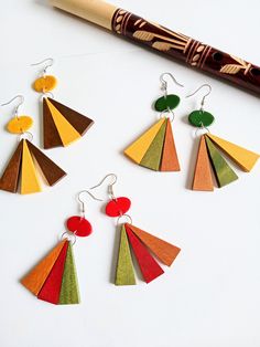 four different colored wooden earrings on a white surface next to a crayon pencil