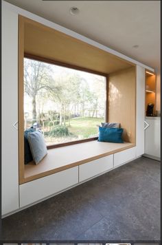 a window seat with pillows on it in front of a large window that looks out onto a field