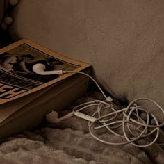 an open book laying on top of a bed next to headphones and wires in it