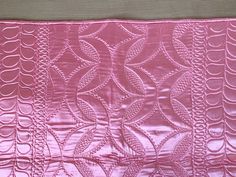 a close up of a pink quilt on a wooden tablecloth with an intricate design