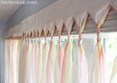 pink and yellow curtains hanging from the side of a window with white drapes on them