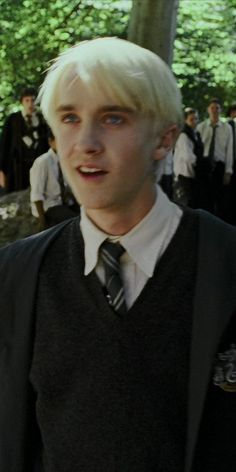 a young man with white hair wearing a vest and tie in front of a group of people