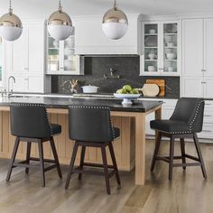 a kitchen with white cabinets and black counter tops, two stools at the island