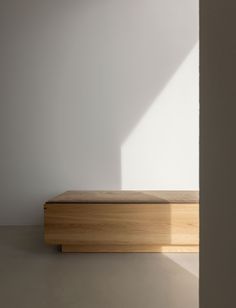 a wooden bench sitting in the middle of a room next to a white wall and window