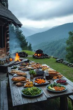 a table full of food on the side of a mountain with a fire in the background