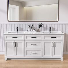 a white bathroom vanity with two sinks and a large mirror over the top that hangs above it