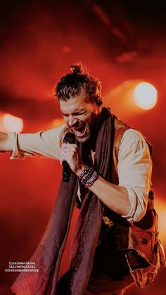 a man singing into a microphone while holding a scarf around his neck and wearing a vest