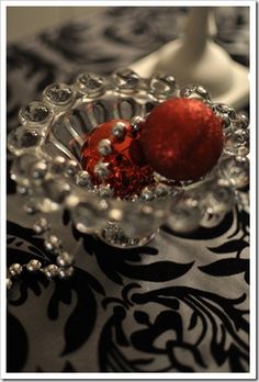 a red ball in a glass bowl on a black and white table cloth with silver beads