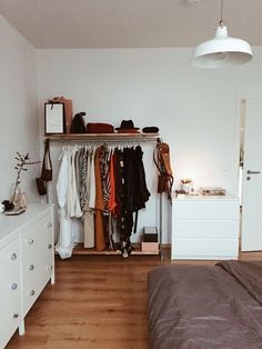 a bedroom with a bed, dresser and hanging clothes on the rack in front of it