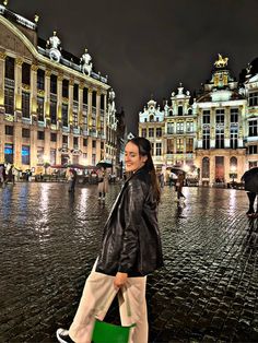 a woman is walking down the street in front of some buildings at night with her green handbag