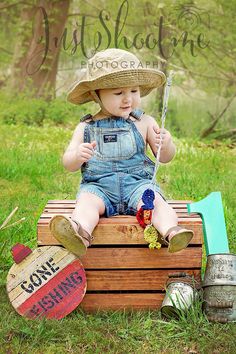 a little boy sitting on top of a wooden crate in the grass wearing a hat