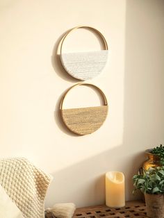 two circular wall hangings are on the wall next to a candle and potted plant