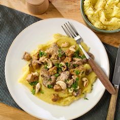 a white plate topped with mashed potatoes covered in meat and veggies next to a fork