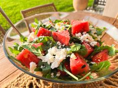 a salad with watermelon, feta cheese and spinach in a glass bowl