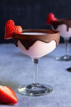 two glasses filled with chocolate and strawberries on top of a blue table cloth next to each other