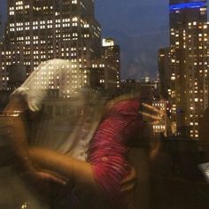 two people standing on top of a building at night with city lights in the background