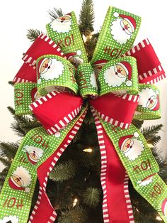 a green and red christmas tree bow with santa clause on it's head, hanging from the top of a pine tree