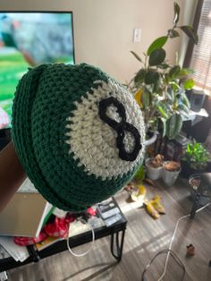 a green and white crocheted hat with the letter b on it sitting in front of a television