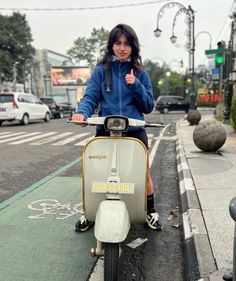 a woman riding on the back of a scooter down a street next to a sidewalk