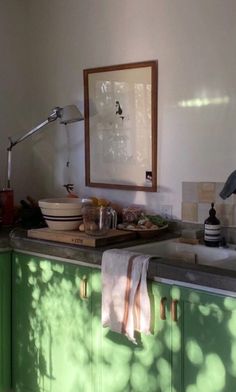 a kitchen with green cabinetry and counter tops under a framed art work on the wall