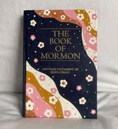 the book of mormon on a bed with white sheets and pink, gold and blue flowers