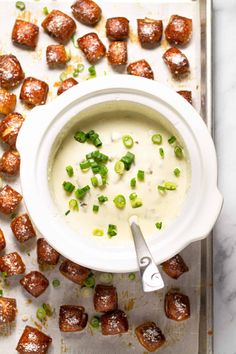 a white bowl filled with soup next to small bites of meatballs on a baking sheet