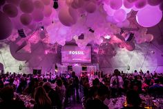 a large group of people sitting at tables in a tent with balloons hanging from the ceiling