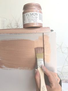 a person holding a paintbrush in front of a wall with some beige paint on it