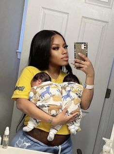 a woman holding a baby taking a selfie in the bathroom mirror with her cell phone