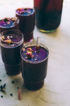 three glasses filled with purple liquid sitting on top of a white table next to bottles