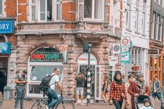 people are walking and riding bikes in front of stores on a city street with tall brick buildings