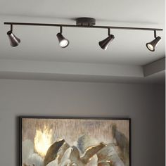 three lights are hanging from the ceiling above a painting in a room with gray walls