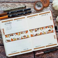 an open planner sitting on top of a wooden table next to some pens and pencils