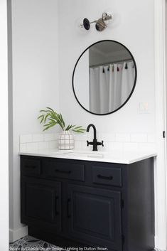 a black and white bathroom with a round mirror on the wall above the sink, along with a potted plant