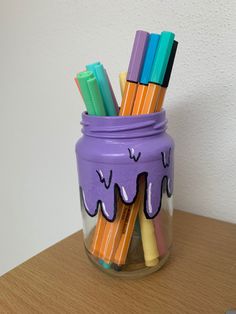 a jar filled with lots of different colored pencils on top of a wooden table