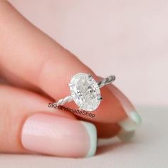 a woman's hand holding a ring with a white diamond in the middle, on top of her finger