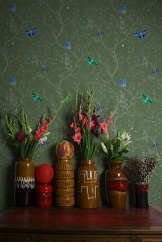 there are vases with flowers and plants on the table next to each other in front of a green wall