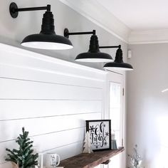 three lights hanging from the ceiling above a mantle in a white room with christmas decorations