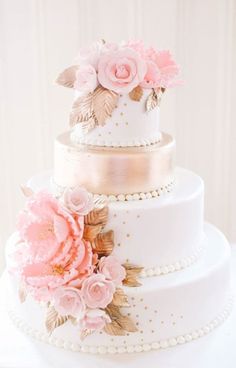 a three tiered wedding cake with pink flowers on the top and gold trimmings