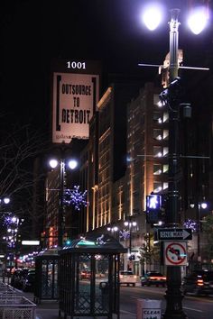 a city street at night with lights and signs on the side of the road that read, out space to detrott