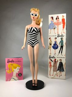 a barbie doll is posed next to an old fashion book