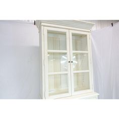 a white china cabinet with glass doors on the top and bottom, in front of a wall